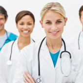 Beautiful young doctor standing with hands folded and assistant doctors in background