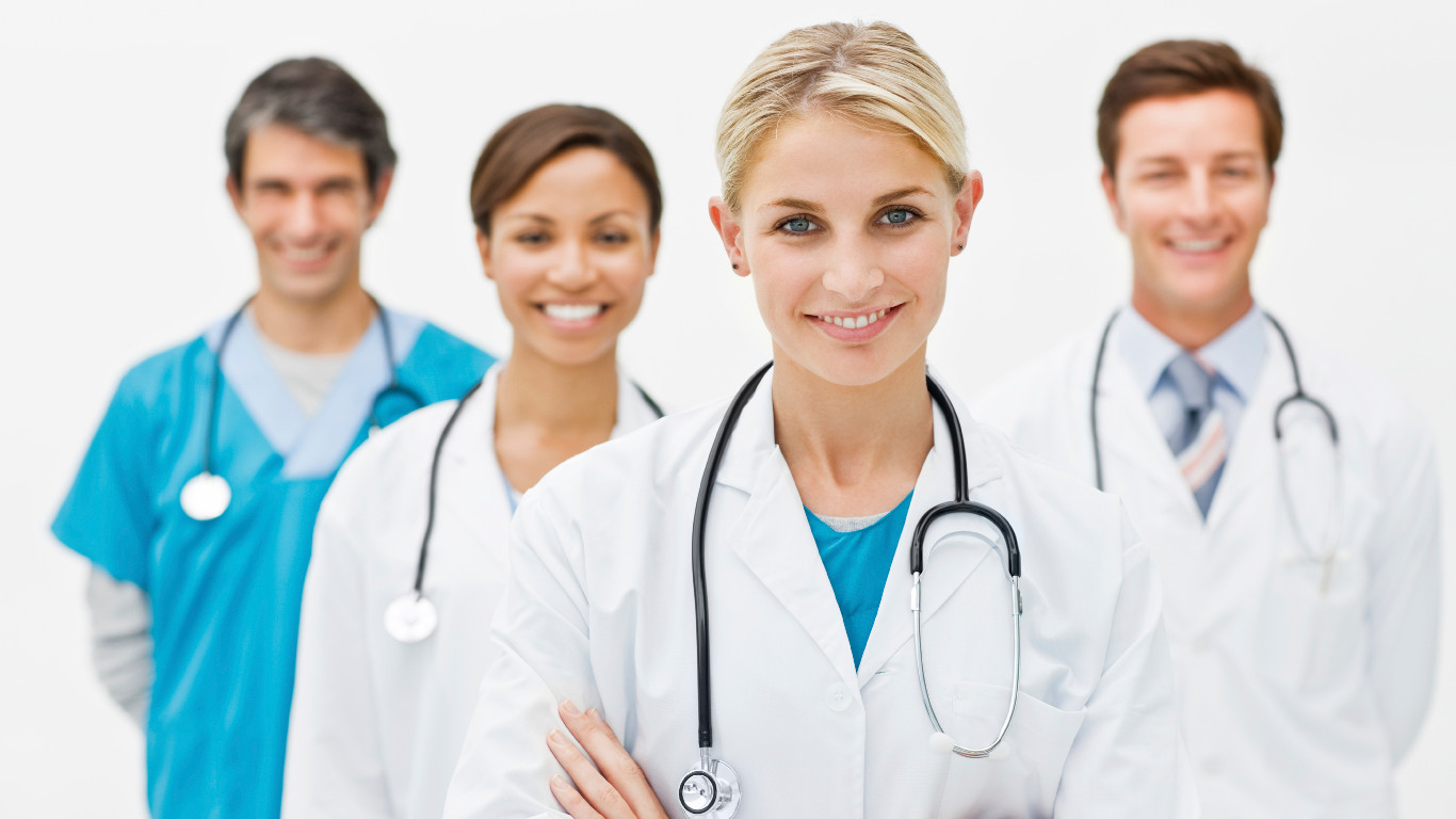Beautiful young doctor standing with hands folded and assistant doctors in background