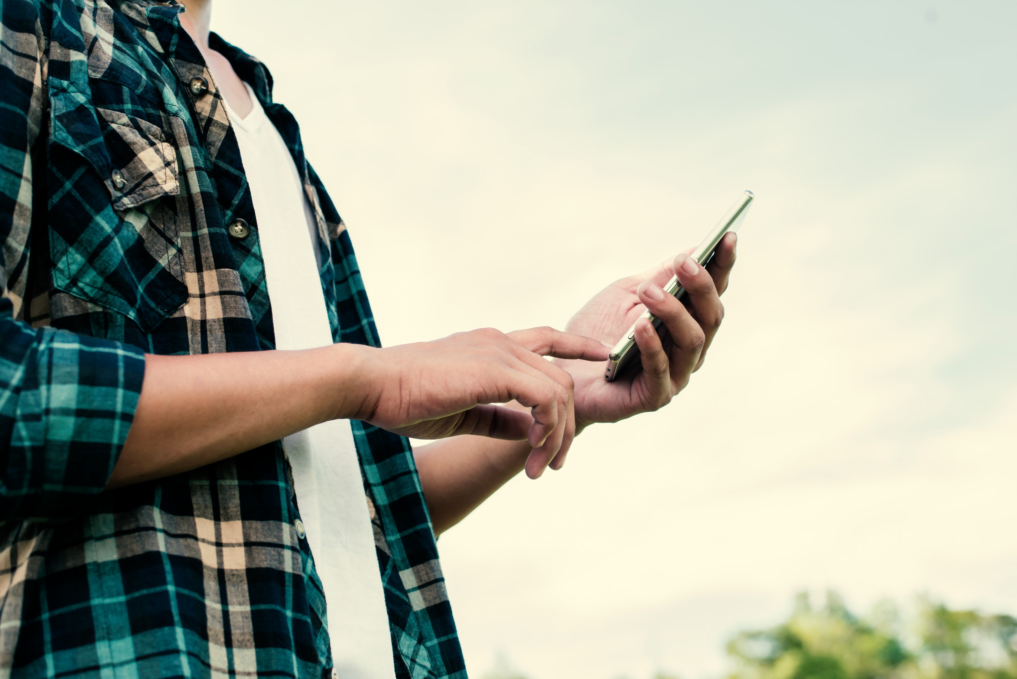 Close-up of hipster man hands using his smartphone outdoor in the park.